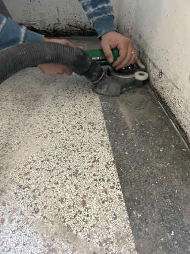 Slijpen van Terrazzo Een persoon maakt een vloer schoon met een stofzuiger in een hoek van de kamer.