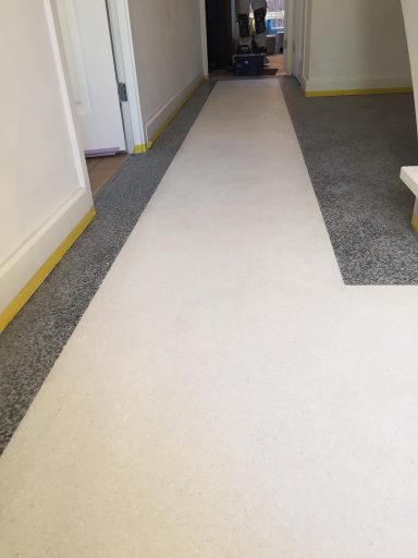 terrazzo vloer Lange gang met een lichte vloerbedekking en gele plinten aan de zijkanten.