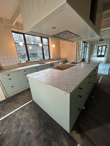 granito keukenblad Moderne keuken met een groen keukeneiland en marmeren blad, nog in aanbouw.